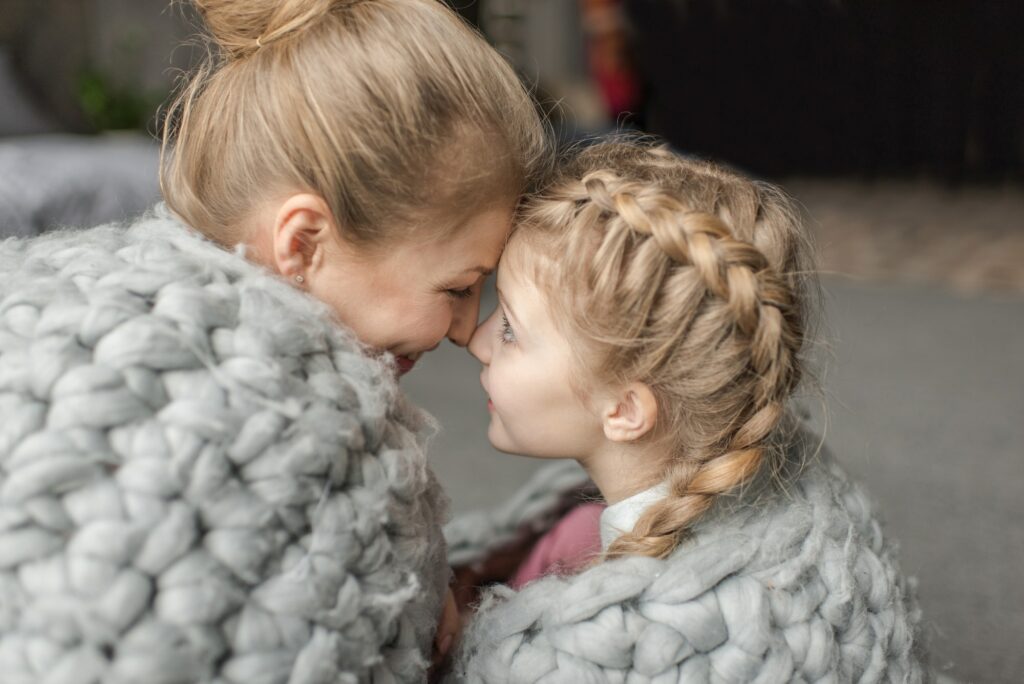 Beautiful happy mother and daughter sitting together under merino wool blanket